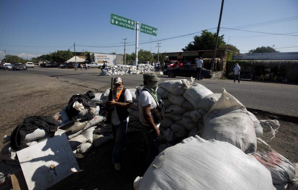 Men belonging to the Self-Defense Council of Michoacan, (CAM), stand guard at a checkpoint in the entrance to the town of Nueva Italia, Mexico, Monday, Jan. 13, 2014. A day earlier the self-defenses encountered resistance as they tried to rid the town of the Knights Templar drug cartel while the government announced today that federal forces will take over security in a large swath of a western Mexico that has been hard hit by violence. (AP Photo/Eduardo Verdugo)