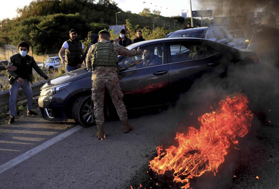 A Lebanese soldier asks a driver to move away from burning tires that were set on fire by protesters to block a highway that leads to Beirut's international airport, in Beirut, Lebanon, Tuesday, March 2, 2021. Scattered protests broke out in different parts of Lebanon Tuesday after the Lebanese pound hit a record low against the dollar on the black market, a sign of the country's multiple crises deepening with no prospects for a new Cabinet in the near future. (AP Photo/Hussein Malla)