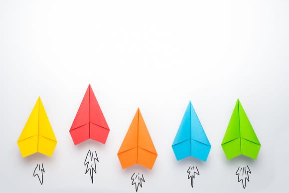 Paper airplanes of different colors are lined up in a row, with illustrations of flames coming out from behind them, as if they're rockets.