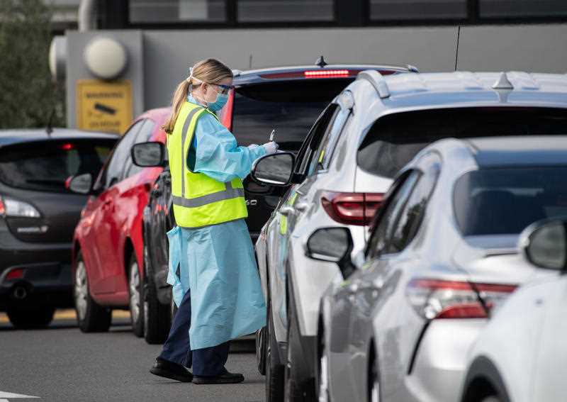 NSW Health workers dressed in Personal Protective Equipment (PPE) are seen collecting information as people wait in their cars to receive coronavirus testing at the Crossroads Hotel in Sydney.