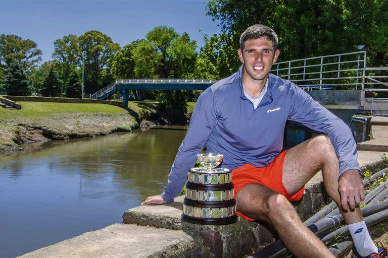 Delbonis, en su ciudad, con el arroyo Azul detrás y la réplica de la Copa Davis que atesora en su casa