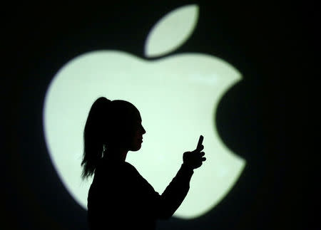 Silhouette of mobile user is seen next to a screen projection of Apple logo in this picture illustration taken March 28, 2018. REUTERS/Dado Ruvic/Illustration