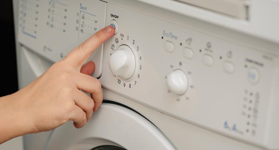 Woman's hand shown turning on power on an older-style washing machine.