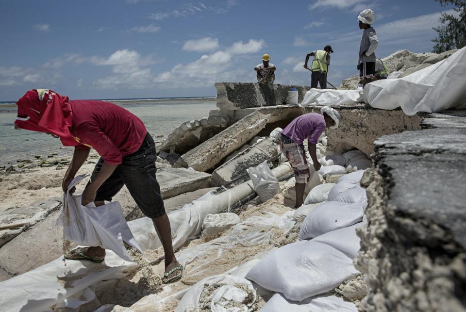 Men laying sandbags along a coastal road in Kiribati that was damaged by flooding related to sea level rise.