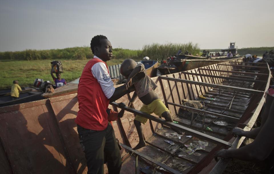 A man who arrived a number of days earlier helps a young newly arrived displaced boy from a river barge, some of the thousands who fled the recent fighting between government and rebel forces in Bor by boat across the White Nile, in the town of Awerial, South Sudan Thursday, Jan. 2, 2014. The international Red Cross said Wednesday that the road from Bor to the nearby Awerial area "is lined with thousands of people" waiting for boats so they could cross the Nile River and that the gathering of displaced is "is the largest single identified concentration of displaced people in the country so far". (AP Photo/Ben Curtis)