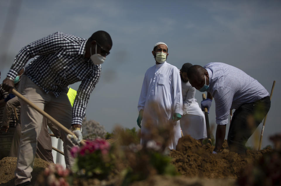Mourners shovel dirt onto the grave of a Guinean man, who died of COVID-19 and who the family did not wish to identify by name, during a funeral at the cemetery of Evere, Belgium, Friday, April 24, 2020. Shops and restaurants in Belgium remain closed and weddings and funerals are limited in number during a partial lockdown to prevent the spread of the coronavirus. (AP Photo/Virginia Mayo)