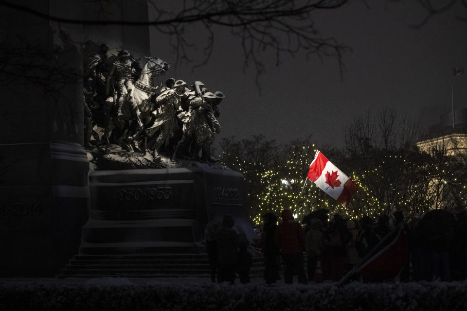 Protesters fly the Canadian flag as they stand by the Tomb of the Unknown Soldier at the National War Memorial on the 21st day of a protest against COVID-19 measures that has grown into a broader anti-government protest, on Thursday, Feb. 17, 2022, in Ottawa. (Justin Tang/The Canadian Press via AP)