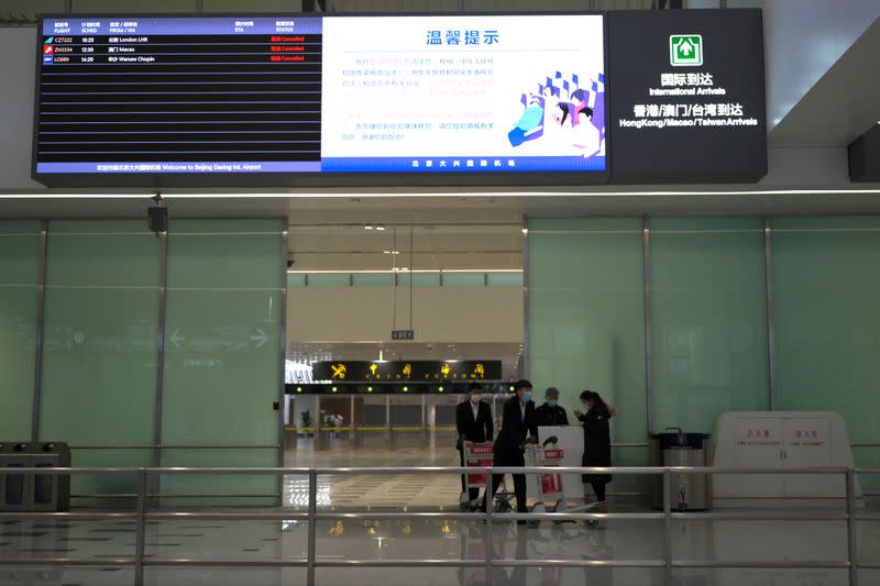 Staff members wear face masks at the International Arrival gate with an information board showing cancelled flights, at the Beijing Daxing International Airport, as the country is hit by an outbreak of the novel coronavirus, in Beijing