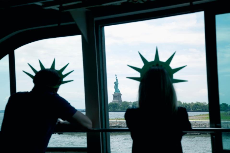 Couple wearing liberty crowns viewing distant Statue of Liberty while aboard a ferry