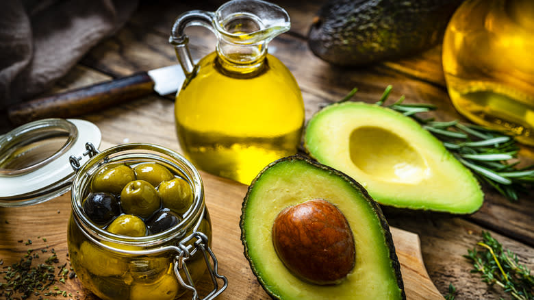 Jar of olives in oil and avocado halves near a glass jug of oil