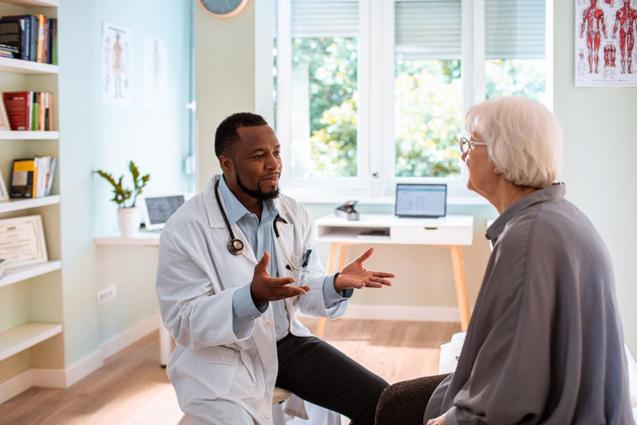 Male physician sitting and talking with a senior female patient in a modern exam room with a trendy desk and decor