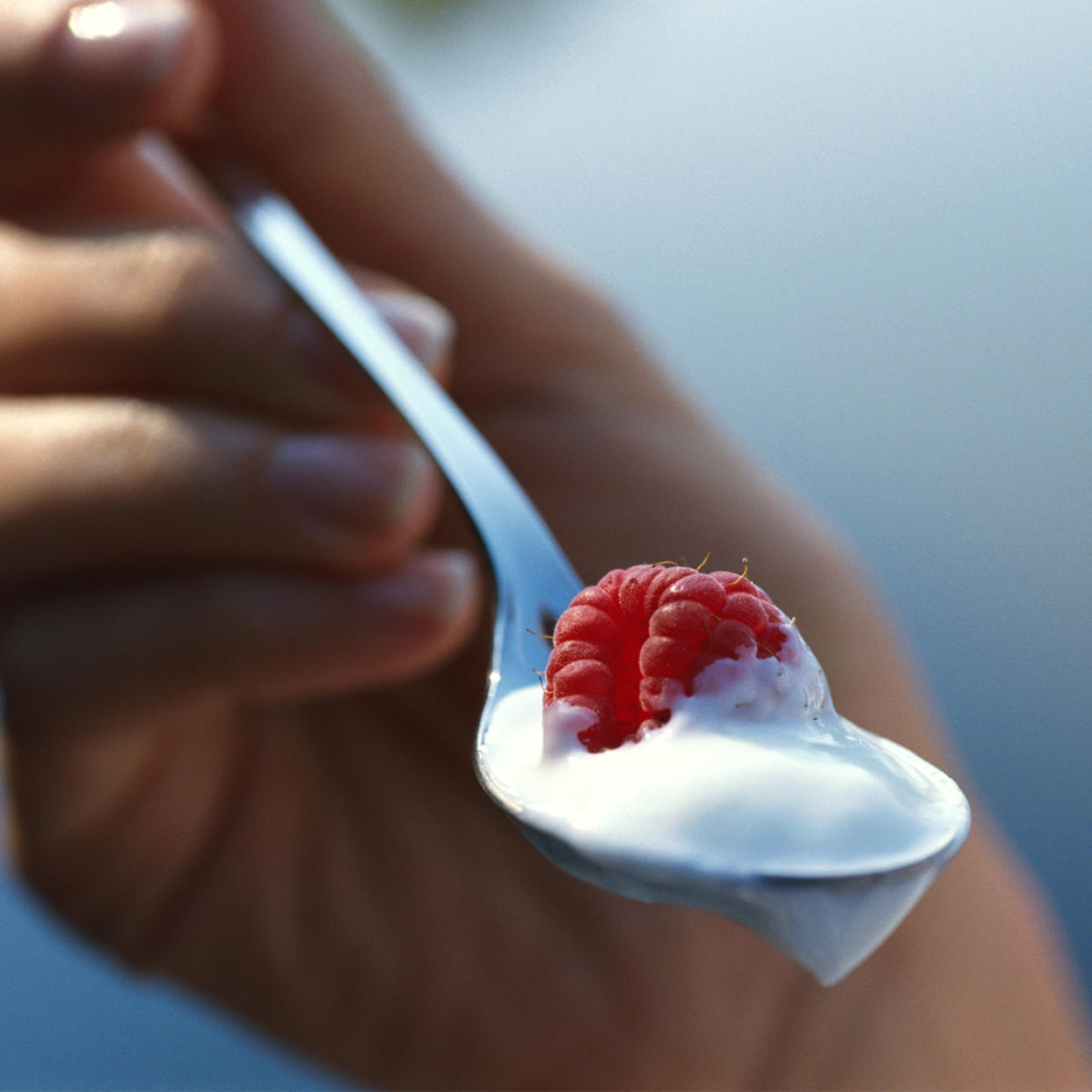 womans hands with a spoon of yogurt and raspberry