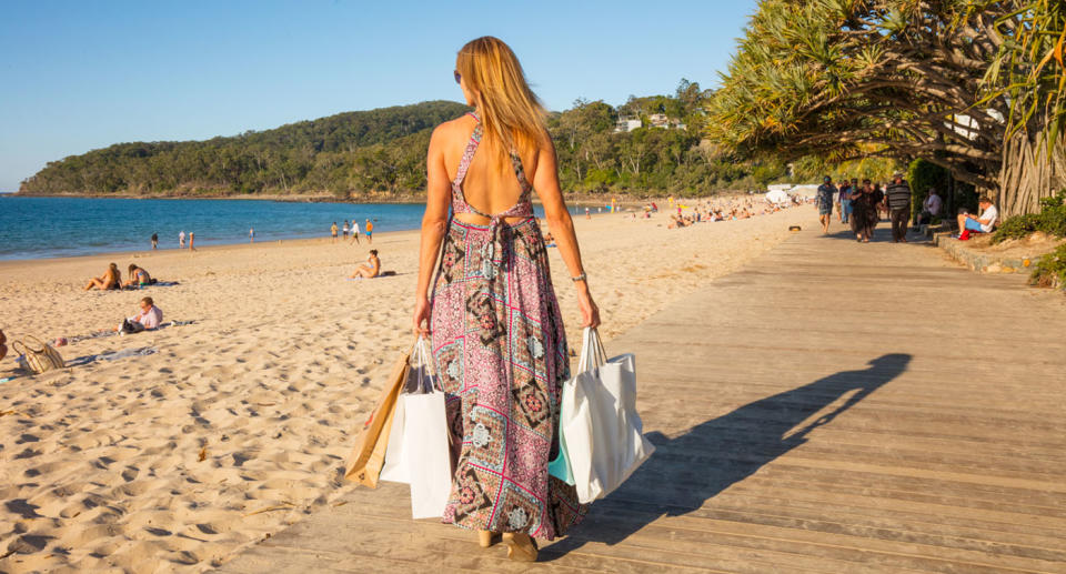 A woman walks along the boardwalk in Noosa with shopping bags.