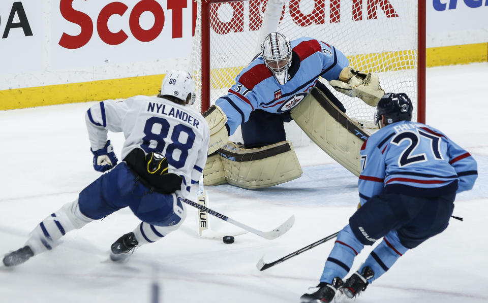 Winnipeg Jets goaltender Connor Hellebuyck (37) poke checks Toronto Maple Leafs' William Nylander (88) as Nikolaj Ehlers (27) looks on during the second period of an NHL hockey game, Saturday, Jan. 27, 2024, in Winnipeg, Manitoba. (John Woods/The Canadian Press via AP)