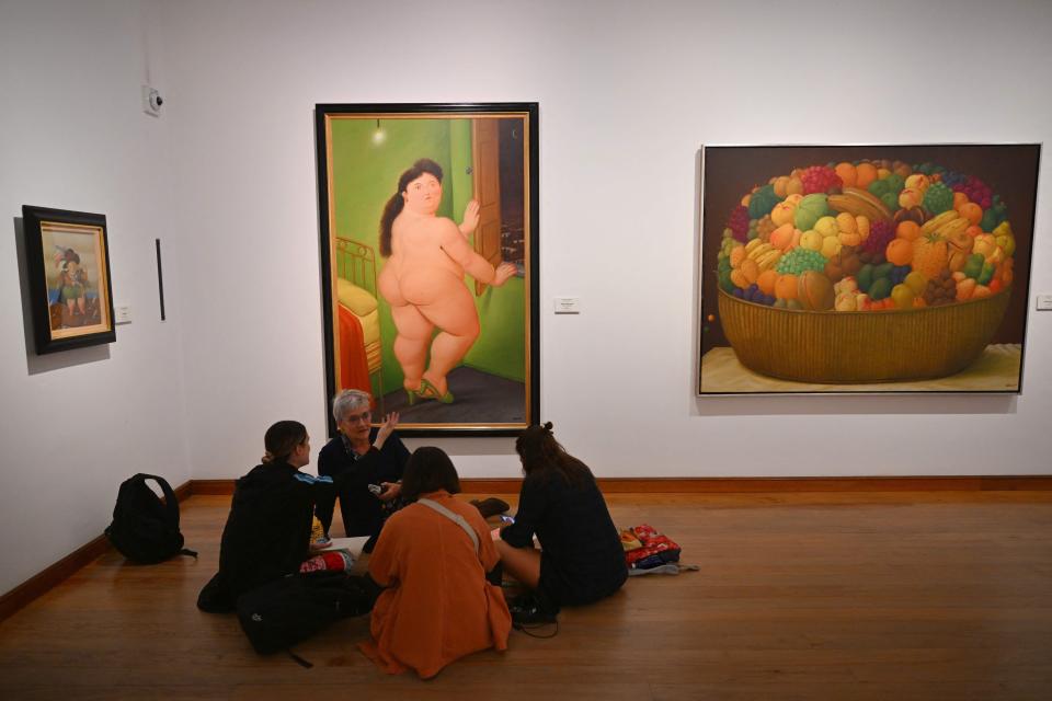 People seat by the painting "Mujer desnuda en una ventana" (Woman Nude by the Window) by Colombian artist Fernando Botero at the Botero Museum in Bogota on Sept. 15, 2023.