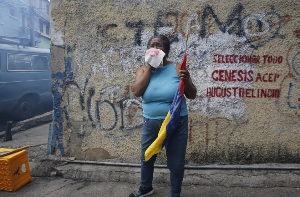 An anti-government protester affected by tear gas, fired by security forces, holds a Venezuelan flag during a show of support for an apparent mutiny by a national guard unit in the Cotiza neighborhood of Caracas, Venezuela, Monday, Jan. 21, 2019. (AP Photo/Ariana Cubillos)