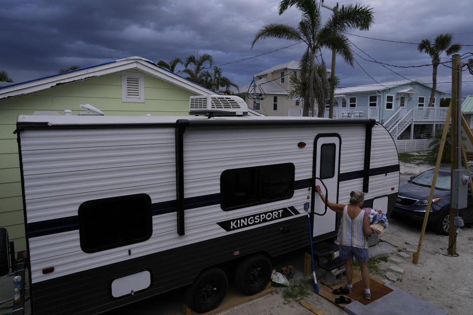 Jacquelyn Velazquez carries laundry, cleaned in an outdoor washing machine and dried on a line, back into the trailer where her family of three is living while waiting to be able to repair their home's leaking roof and rebuild the gutted interior, which flooded nearly to the ceiling during last year's Hurricane Ian, in Fort Myers Beach, Fla., Wednesday, May 24, 2023. After many months renting a small room in a home on the mainland, the Velazquez family received a camper in April from a state assistance program, allowing them to live with their daughter, home from college for the summer, while they wrangle with their insurance company and wait for permits to move forward on repairs. (AP Photo/Rebecca Blackwell)