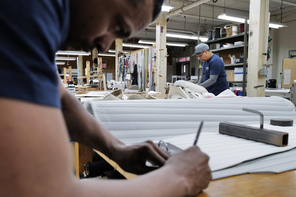 Anthony Pena etches the template for a new section of upholstery, as Cesar Abreu can be seen cutting a section in the background at Cesar Marine Canvas & Upholstery on Harbor Street in New Bedford.