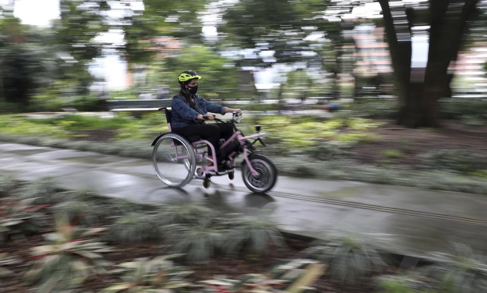 A tourist rides an electric wheelchair during a tour in Medellin, Colombia, Wednesday, Nov. 18, 2020. The steering and breaks on the wheelchairs are like those on a regular bicycle, while accelerating only requires pushing a button on one of the handles. (AP Photo/Fernando Vergara)