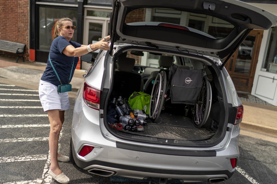 Janet Paulsen holds onto a roof rack as she steps to the back of the car to retrieve her wheelchair before meeting friends for lunch in Acworth, Ga., Tuesday, Aug. 8, 2023. Paulsen has urged the Georgia Legislature to adopt statewide red flag laws to protect vulnerable victims like herself. (AP Photo/David Goldman)