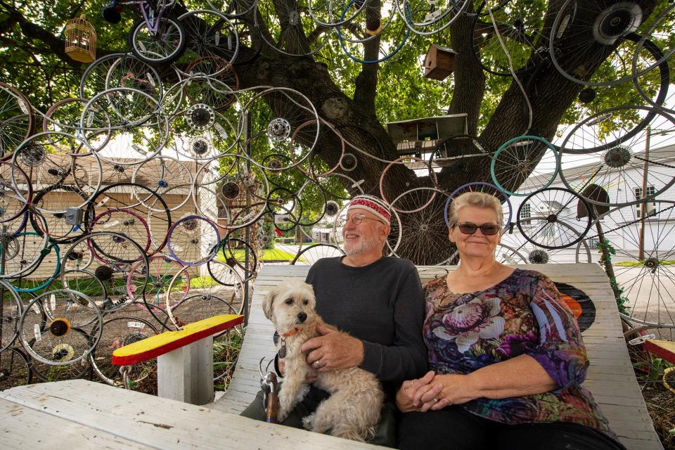 Parker James Hooker, left, and Robin Robinson are surrounded by an arched wall of bicycle rims he calls "Million Miles of Smiles" that fences in their backyard.