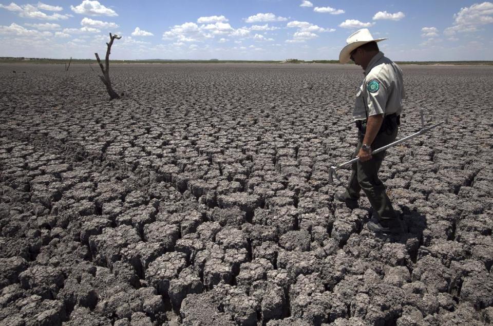 FILE - In this Aug 3, 2011 file photo, Texas State Park police officer Thomas Bigham walks across the cracked lake bed of O.C. Fisher Lake, in San Angelo, Texas. A combination of the long periods of 100 plus degree days and the lack of rain in the drought -stricken region has dried up the lake that once spanned over 5400 acres. From Dallas to far-flung ranches and rice farms, Texans and officials are trying to capitalize on heightened drought awareness by adopting conservation plans that will ease the next crisis. (AP Photo/Tony Gutierrez, File)