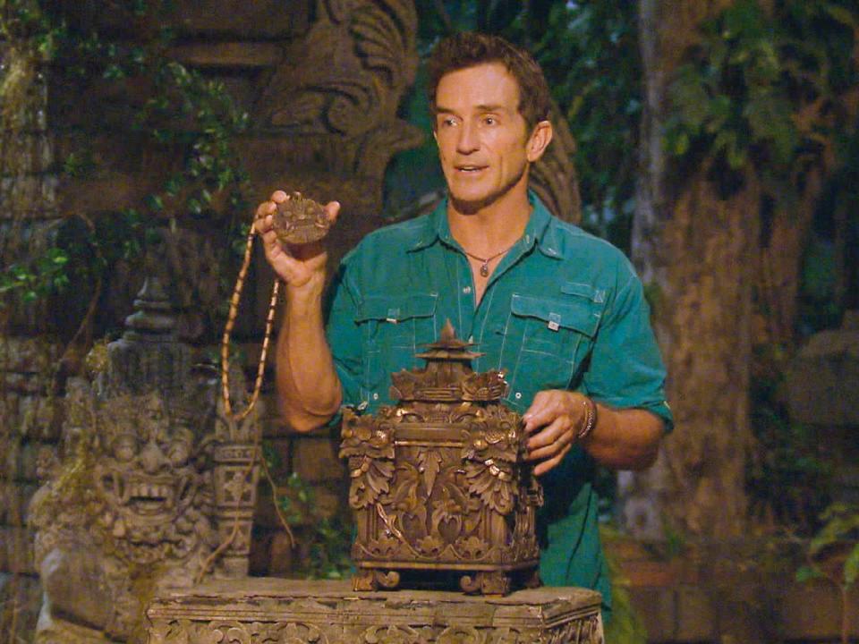 Jeff Probst in a blue shirt holding up a hidden immunity idol on Survivor