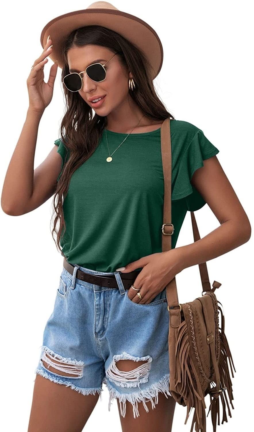 model posing with a hat, sunglasses, green top, denim shorts, and a fringed bag
