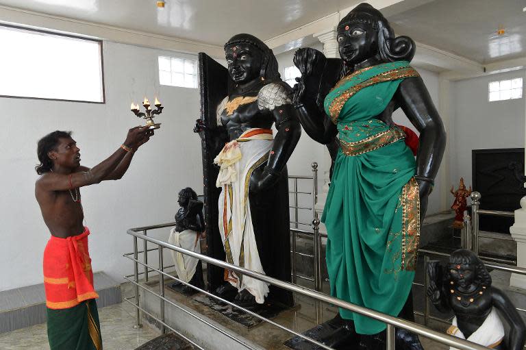 A Hindu priest holds a lit coconut oil lamp in front of statues of Prince Vijaya and demon Princess Kuveni (R) at the Sri Subramaniam temple in Matara on March 7, 2014