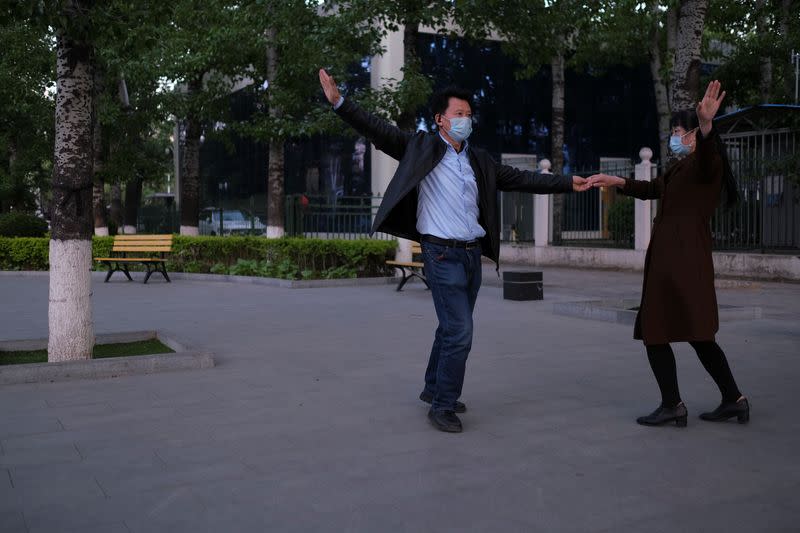 A couple wearing face masks dance at a public square in Beijing,