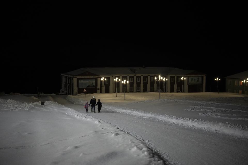 People walk outside during the round-the-clock polar night in Barentsburg, Norway, Saturday, Jan. 7, 2023. (AP Photo/Daniel Cole)