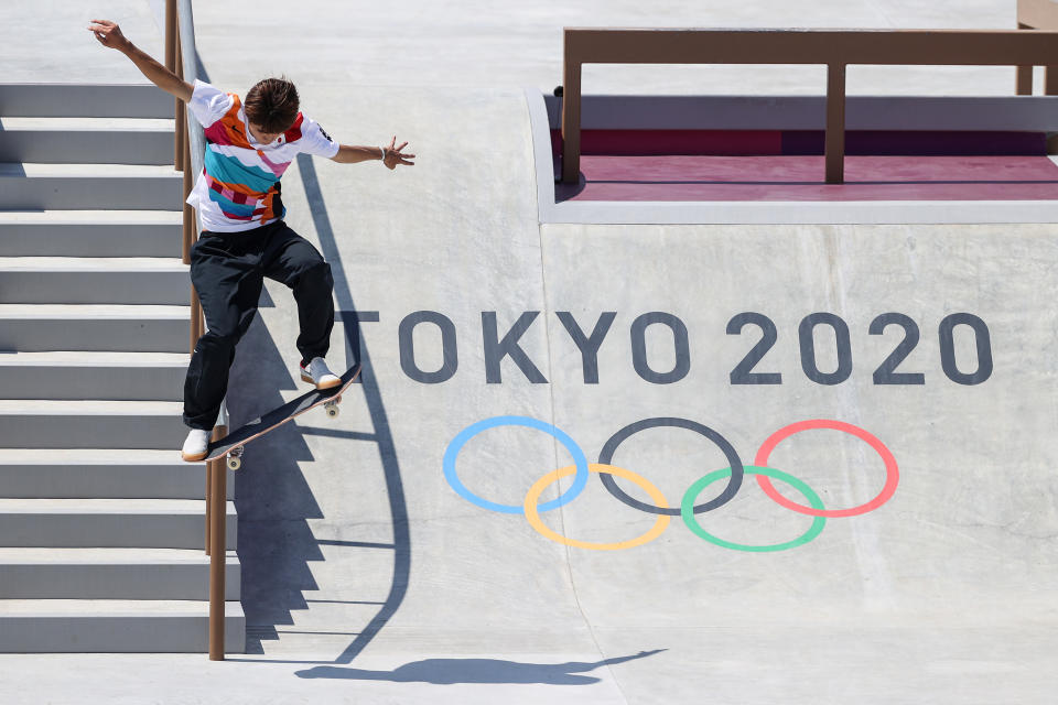 A skateboarder performs a trick down steps in front of the "Tokyo 2020" Olympic logo at a skateboarding event