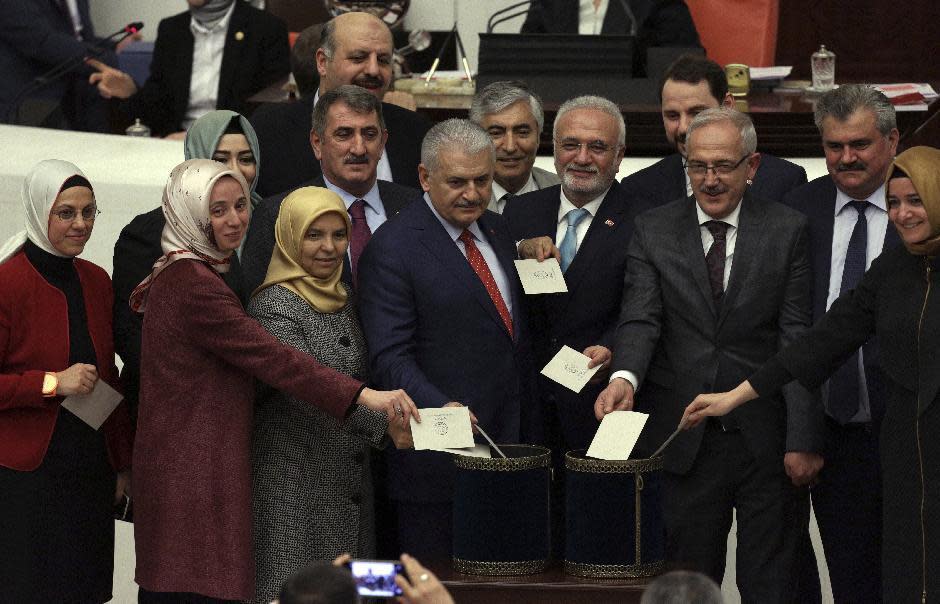 Turkey's Prime Minister Binali Yildirim, center, is surrounded by lawmakers as they cast votes minutes before Turkey's parliament approved a contentious constitutional reform package, paving the way for a referendum on a presidential system that would greatly expand the powers of President Recep Tayyip Erdogan's office, in Ankara, Turkey, early Saturday, Jan. 21, 2017. In an all-night session that ended early Saturday, lawmakers voted in favor of a set of amendments presented by the ruling party, founded by Erdogan.(AP Photo/Burhan Ozbilici)