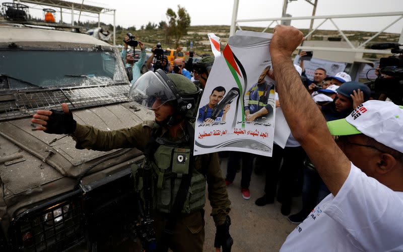 An Israeli soldier gestures as a journalist holds a poster of two journalists that were killed recently in Gaza, during a protest demanding freedom of the press, near Ramallah, in the occupied West Bank