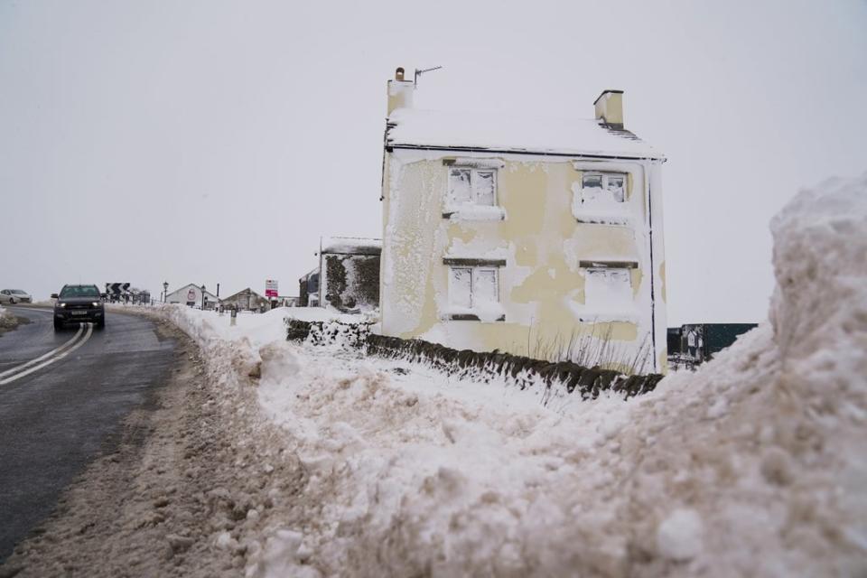 A vehicle passes a house covered in snow on the A53 close to Buxton in Derbyshire (PA)