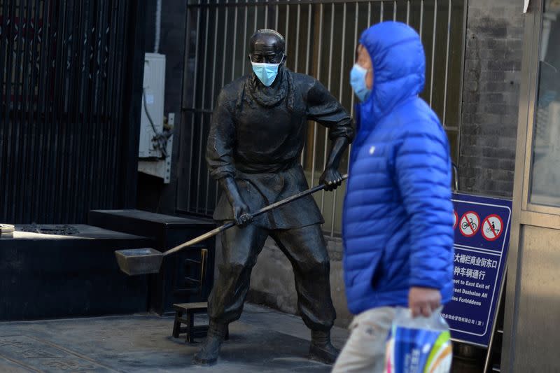 Man wearing a face mask walks past a statue with a face mask on near the Qianmen pedestrian street, following an outbreak of the novel coronavirus in the country, in Beijing