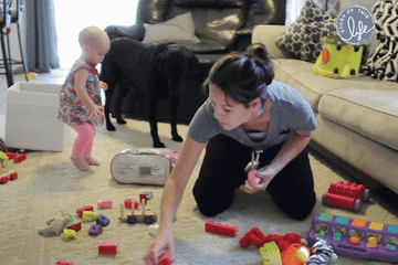 A woman picking up her baby's toys while the baby dumps more on the floor