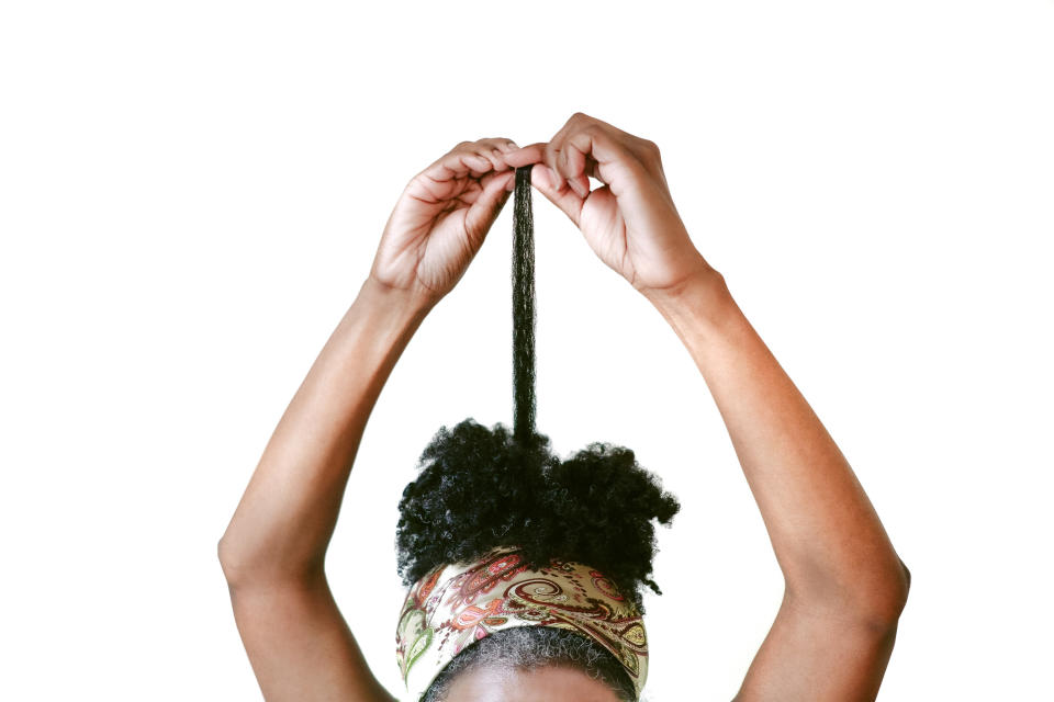 A person with a colorful bandana holds a section of their afro-textured hair stretched above their head, showing its length