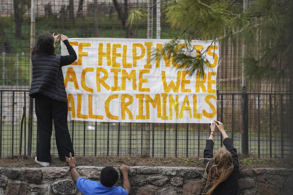 Supporters of the 24 aid workers and volunteers of 24 aid workers and volunteers accused of participating in migrant rescue operations hang up a banner outside the court in Mytilene, on the northeastern Aegean island of Lesbos, Greece, Tuesday, Jan. 10, 2023. A Greek court was set to hear a smuggling-related criminal case Tuesday against a group of 24 aid workers and volunteers. The defendants deny all charges and say all they did was help rescue endangered people. International human rights groups have widely criticized the prosecution. (AP Photo/Panagiotis Balaskas)