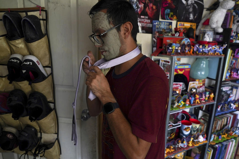 Eliha Rendon, wearing a mood facial mask, tries on a necktie as he prepares to marry his fiancé in a mass wedding ceremony organized by city authorities as part of the LGBT pride month celebrations, in Mexico City, Friday, June 24, 2022. (AP Photo/Fernando Llano)