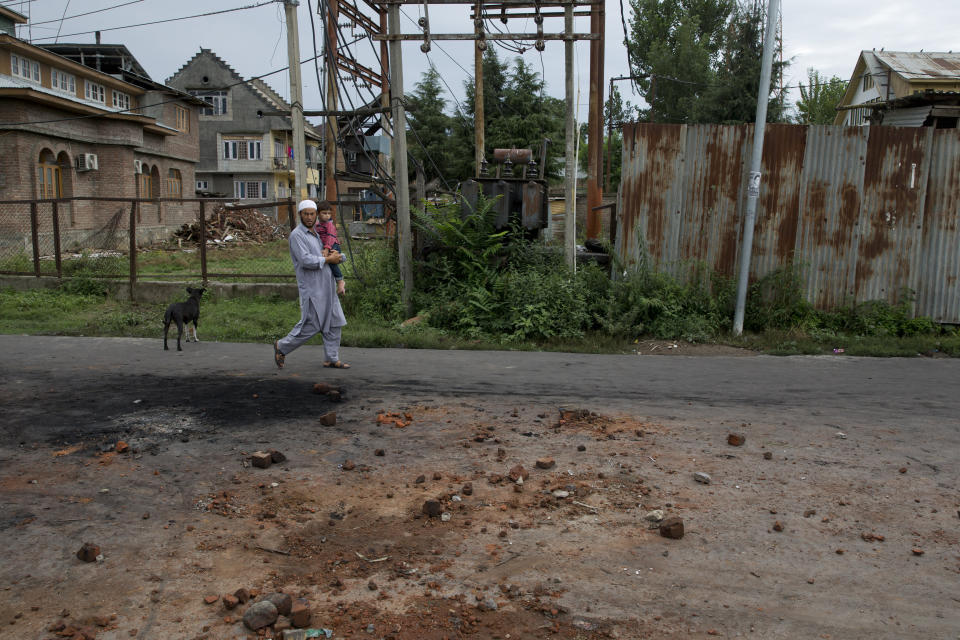 A Kashmiri man carries a child and walks on a road dotted with stones and bricks from earlier protests in Srinagar, Indian controlled Kashmir, Saturday, Aug. 17, 2019. Authorities began restoring landline phone services on Saturday after a nearly two-week security crackdown and news blackout following a decision to downgrade the majority-Muslim region's autonomy. (AP Photo/Dar Yasin)