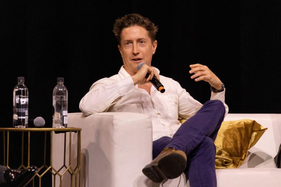david gordon green, a man wearing a white button down shirt and purple pants, holding a microphone while speaking on stage
