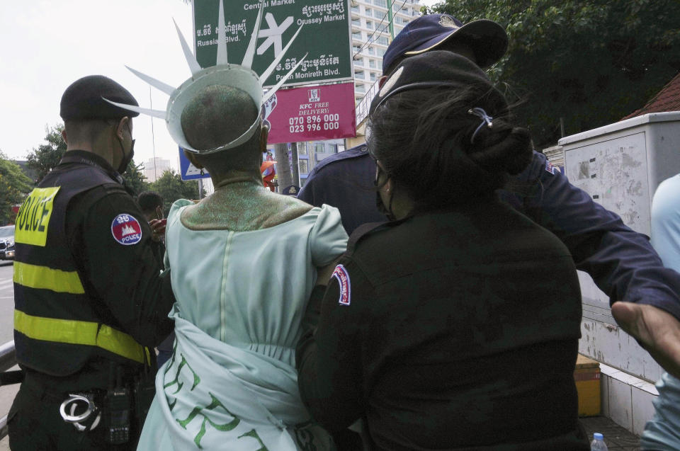 Cambodian-American lawyer Theary Seng, center, dressed in the Lady Liberty, is escorted by local police officers outside Phnom Penh Municipal Court in Phnom Penh, Cambodia, Tuesday, June 14, 2022. The Cambodian American lawyer and dozens of members of a now-dissolved opposition party were convicted of treason Tuesday in a trial that was the latest move to tame all opposition to the long-running rule of Prime Minister Hun Sen. (AP Photo/Heng Sinith)