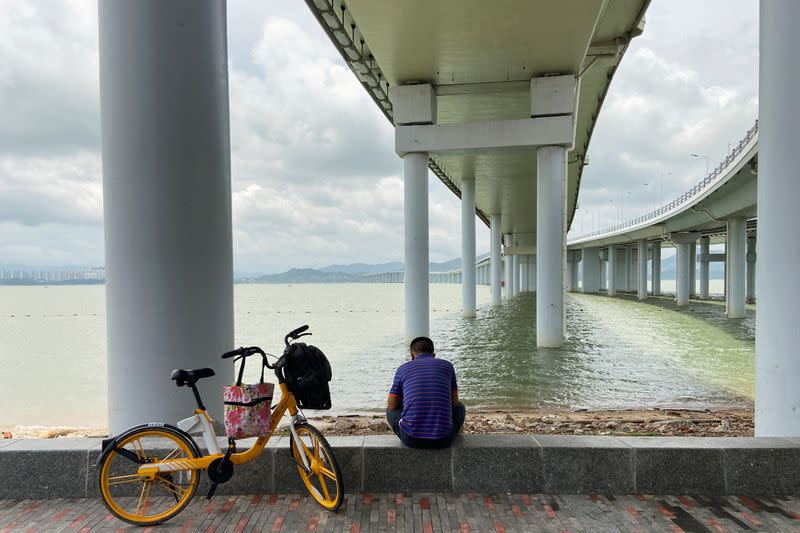 Man sits under a bridge leading to Hong Kong, in Shenzhen