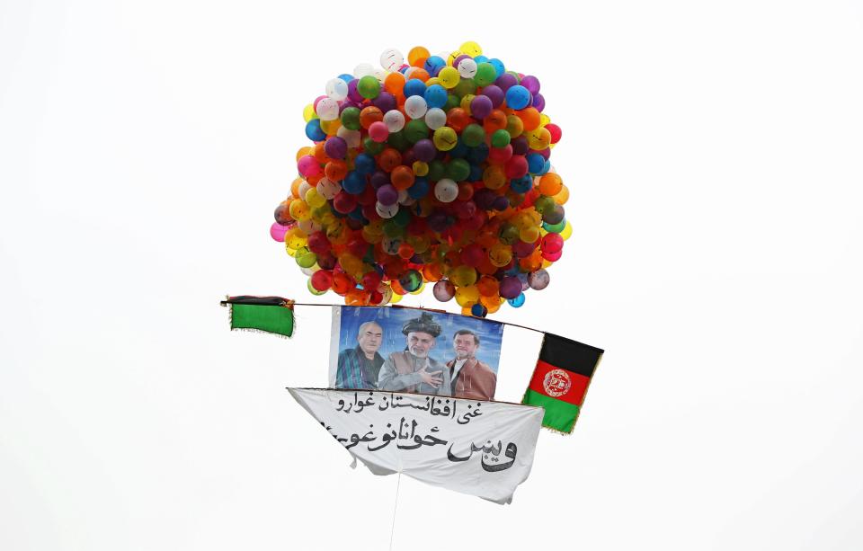 In this photo taken on Tuesday, April 1, 2014, balloons lift a poster of Afghan presidential candidate Ashraf Ghani Ahmadzai skyward during a campaign rally in Kabul, Afghanistan. Writing on the poster reads, "We want a reach Afghanistan, we want talented youth." (AP Photo/Massoud Hossaini)