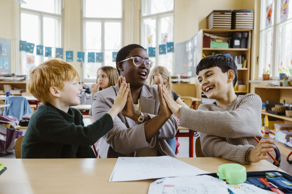 Teacher and students are engaged in a joyful high-five at a classroom desk