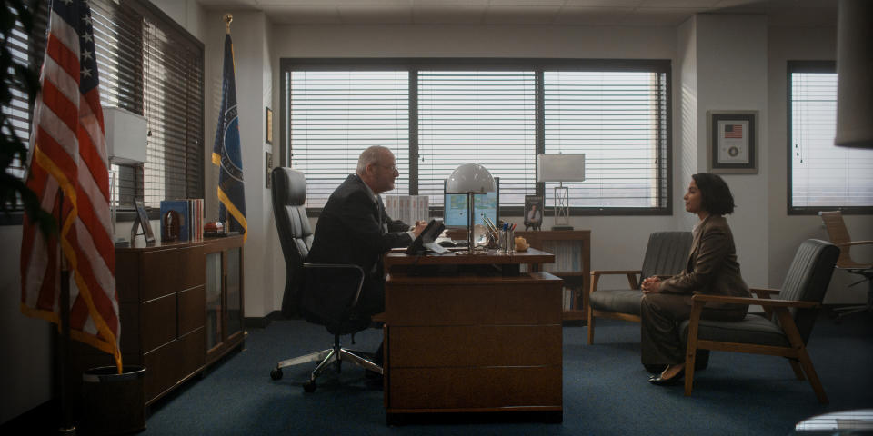 two people sit in an office on opposite sides of a large wooden desk