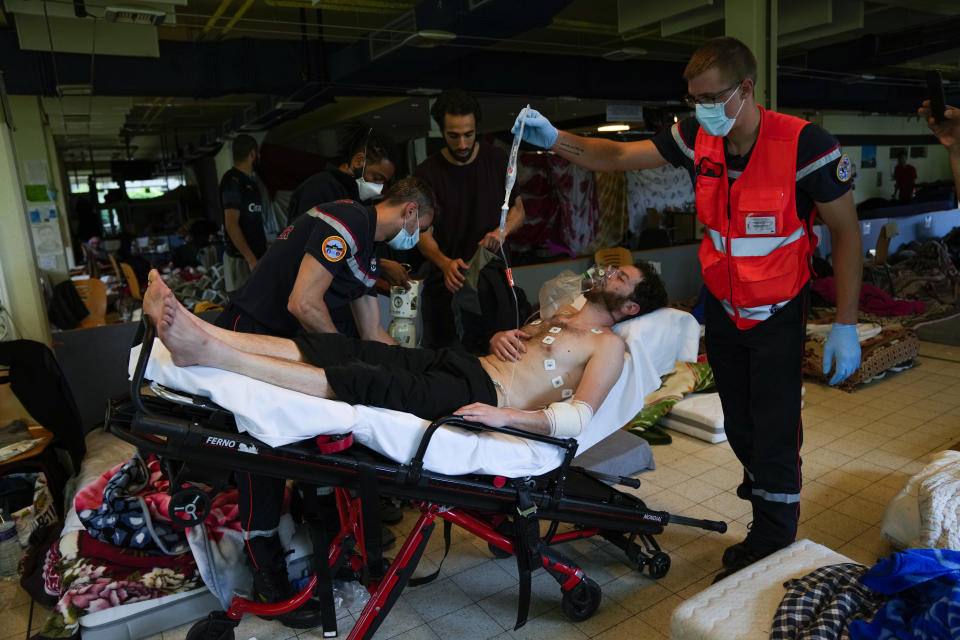 Firefighters and Red Cross health workers attend a man on hunger strike to be transferred to a hospital as he occupies with others a big room of the ULB Francophone university in Brussels, Tuesday, June 29, 2021. More than two hundreds of migrants without official papers and who have been occupying a church and two buildings of two Brussels universities since last February, began a hunger strike on 23 May to draw the attention of Brussels authorities to their plight. (AP Photo/Francisco Seco)