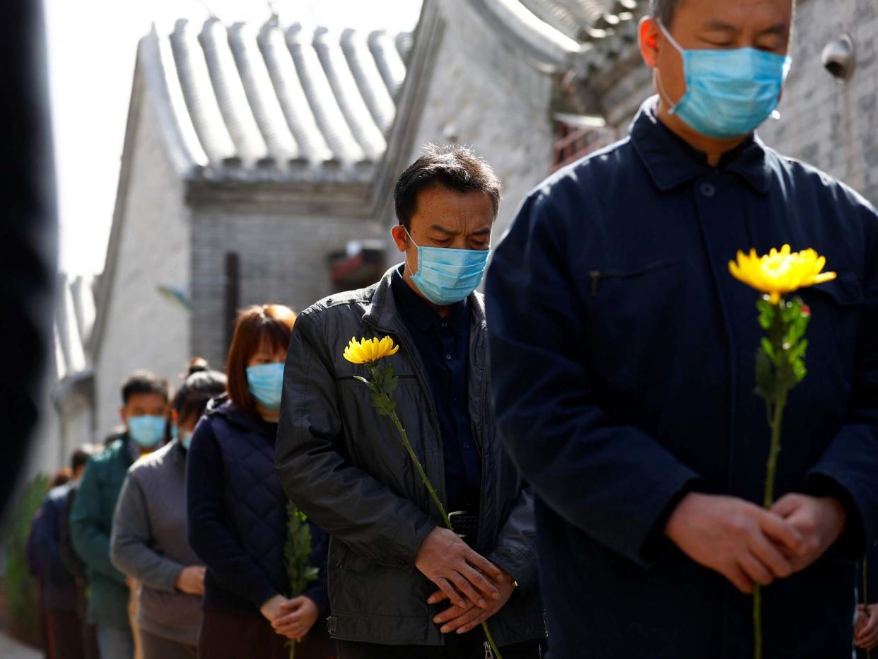 People holding flowers observe a moment of silence at a memorial event in Beijing for those lost to the coronavirus pandemic: Reuters