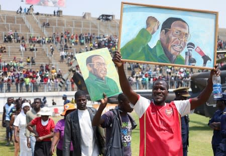 Mourners hold paintings with the face of former Zimbabwean president Robert Mugabe, as they queue to pay their last respects as he lies in state at the at Rufaro stadium, in Mbare